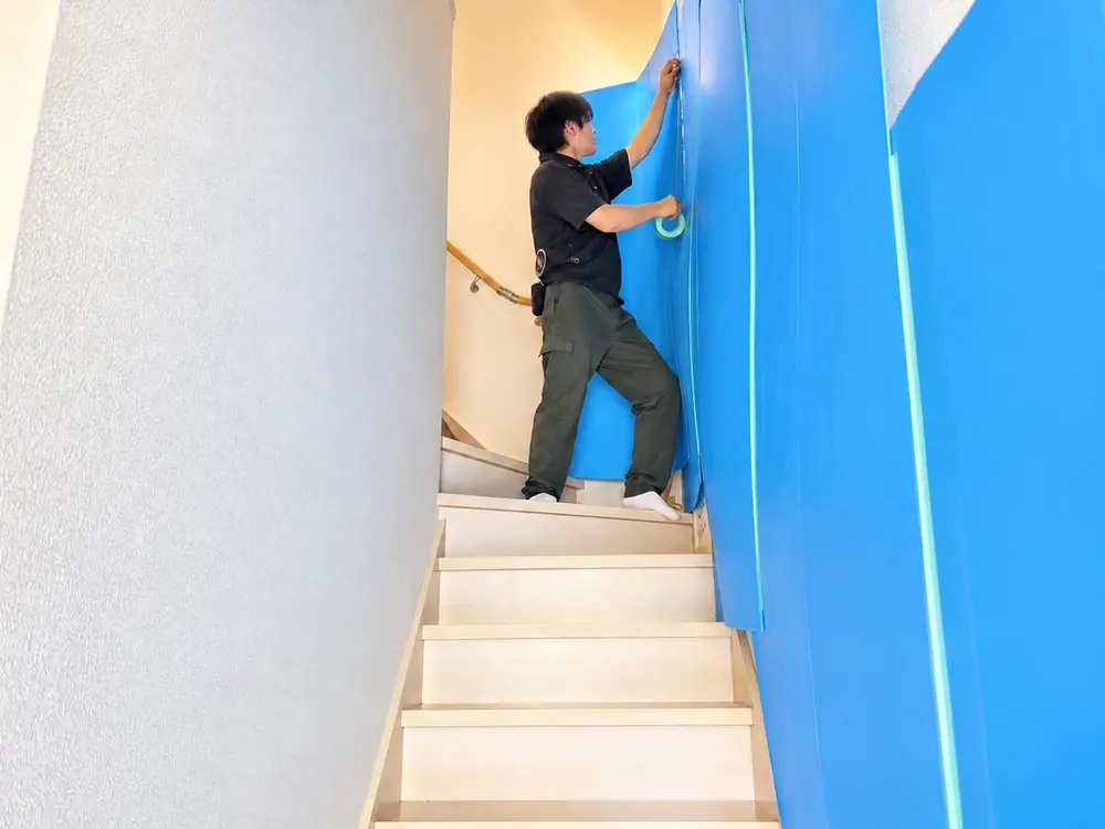 階段の壁を養生材で保護しているスタッフ